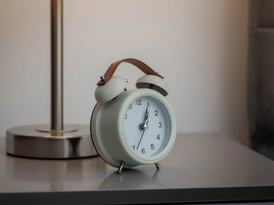 Analog alarm clock and lamp on a nightstand, ready for the clocks to fall back and good sleep